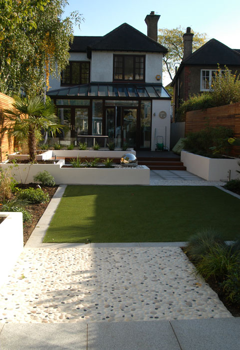 A long Ealing garden with raised beds, granite and pebble paving and artificial lawn